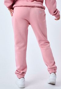 Pantalones de chándal rosas con una textura suave, puños ajustados y un bolsillo trasero. Combinados con zapatillas blancas.