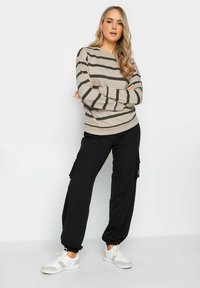 Beige gestreepte sweatshirt met donkere strepen, gecombineerd met zwarte cargo-broeken en witte sneakers. Zachte textuur en een ontspannen fitting.