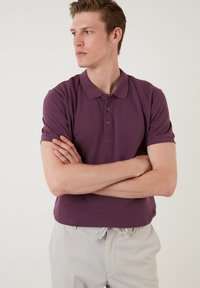 T-paita lyhythihainen tumman violetin värisenä, jossa on klassinen kaulus ja kolmesta napista koostuva napitus, valmistettu teksturoidusta kankaasta.