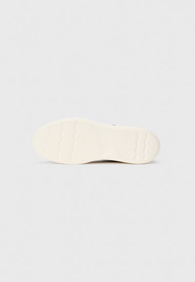 White rubber sole of a casual sneaker with wavy tread pattern, photographed from the bottom on a plain light background.