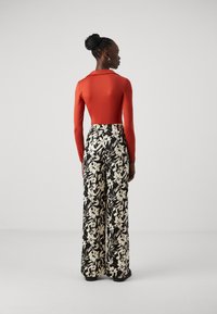 Rød langermet body, kombinert med sorte bukser med bred ben som har et hvitt blomstermønster. Bodyen har en tettsittende overdel og buksen har strikk i livet.