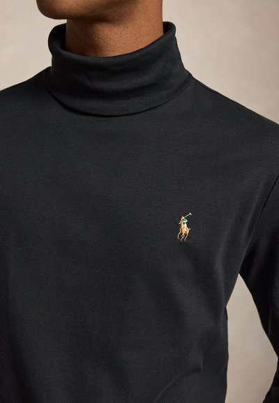 Muž v čiernom roláku s malým vyšitým logom hráča póla na koni na ľavej strane hrude.