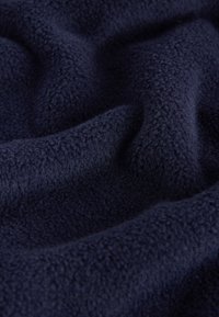 Marineblauer Fleece-Stoff mit einer weichen, strukturierten Oberfläche, der wellenförmige Falten zeigt und ein gleichmäßiges, flauschiges Erscheinungsbild hat.