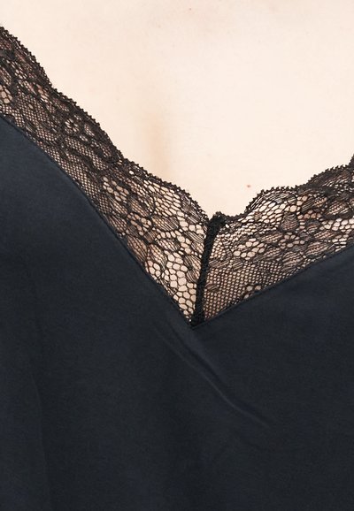 Μαύρο τοπ με V-λαιμόκοψη, διακοσμημένο με λεπτομερή λουλουδάτη δαντέλα σε ανοιχτόχρωμο δέρμα.