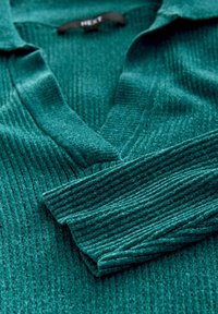 Teal ribbed knit long-sleeve sweater with a deep V-neck collar, folded sleeves, and a visible brand label inside the neckline.