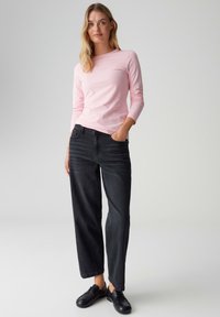 Hellrosa langärmliges Hemd kombiniert mit locker sitzender schwarzer Jeans, mit klassischem Design und dezenter Textur, ergänzt durch schwarze Schuhe.