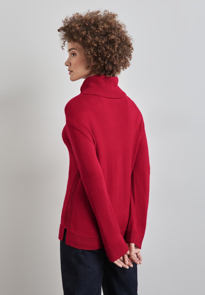 Roter Rollkragenpullover mit geripptem Muster, seitlichen Schlitzen und langen Ärmeln. Glattes Material, lockerer Schnitt und kontrastierendes Kragendetail.