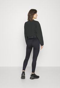 Felpa nera cropped con maniche lunghe abbinata a leggings neri a vita alta. Scarpe da ginnastica nere completano l'outfit.