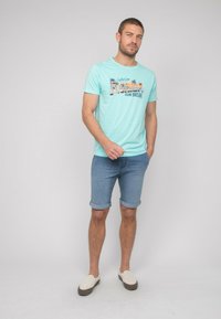 T-shirt bleu clair avec un graphisme "Florida Sun Break", associé à un short en denim roulé et des chaussures légères à enfiler.