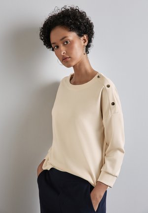 Cream-colored long-sleeve top with a round neckline and button accents on shoulders, crafted from soft material, features a relaxed fit.