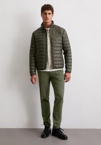 Oliwkowo-zielona pikowana kurtka ze stójką, zestawiona z jasnobeżową koszulą i oliwkowo-zielonymi spodniami. Całość dopełniają czarne sznurowane buty.