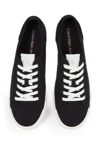 Poros juodų drobinių sportbačių su baltais raišteliais ir padais, "Calvin Klein Jeans" ženklinimas ant liežuvėlio ir vidpadžio, žiūrint iš viršaus.