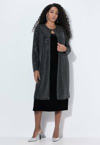 Vestido de terciopelo negro con un cárdigan largo, abierto por delante, cubierto de lentejuelas plateadas. Cuello alto y mangas tres cuartos. Tacones plateados completan el conjunto.