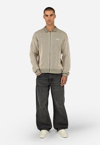 Šviesiai ruda, vertikaliai dryžuota megztinis su apykakle ir raukiniais ant rankovių, derinamas su laisvais juodais džinsais ir baltais sportbačiais.