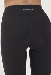 Czarne legginsy sportowe z wysokim stanem, z okrągłym wycięciem z tyłu. Materiał jest gładki i elastyczny.