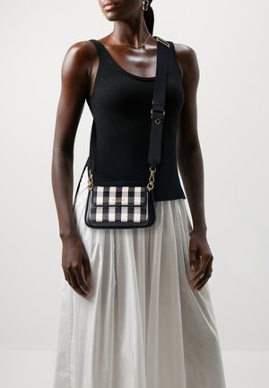 Black and white checkered crossbody bag with gold hardware and a black strap, paired with a fitted black top and white skirt.