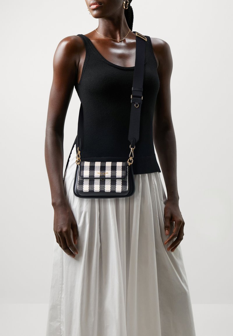 Sac en bandoulière à carreaux noir et blanc avec quincaillerie dorée et une sangle noire, associé à un haut noir ajusté et une jupe blanche.