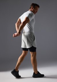 Αθλητική ενδυμασία που περιλαμβάνει κοντομάνικο μπλουζάκι σε ανοιχτό γκρι χρώμα, χαλαρές βερμούδες σε ανοιχτό γκρι χρώμα πάνω από μαύρες κοντές συμπιεστικές βερμούδες, και μαύρα αθλητικά παπούτσια.