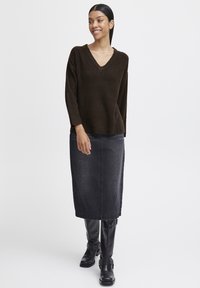 Jersey marrón de canalé con escote en V, combinado con una falda midi de mezclilla negra y botas negras hasta la rodilla con acentos de hebilla.