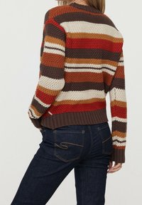 Striped sweater with woven texture in brown, cream, red, and orange. Features a ribbed hem and cuffs. Worn over dark denim jeans.