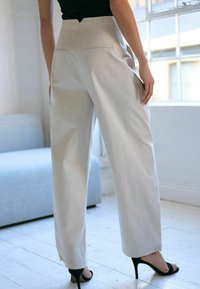Pantalons taille haute de couleur crème en tissu léger, avec une jambe droite, des poches arrière et des détails de couture subtils.