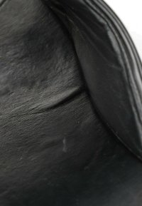 Gros plan d’un matériau en cuir noir avec une texture et des plis visibles, montrant des plis naturels et une surface légèrement brillante.