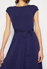 Mörkblå klänning i mjukt tyg, med rundad halsringning, cap sleeves och ett knytbälte i midjan för extra detalj.
