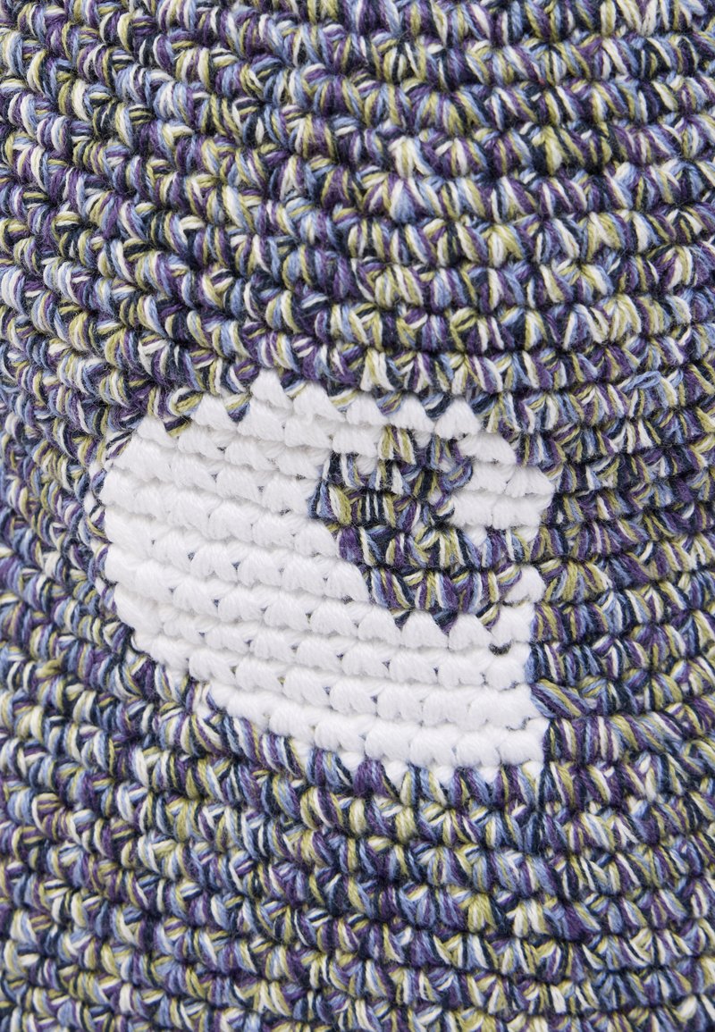 Gros plan sur un tissu au crochet multicolore avec un patch en fil blanc présentant un motif stylisé d'un œil blanc ou d'une bulle de dialogue.