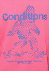 Φωτεινό ροζ πουκάμισο με μπλε σχήμα από τελείες που απεικονίζει έναν περπατώντα άνθρωπο, με το κείμενο "Conditions" πάνω και οδηγίες φροντίδας κάτω.