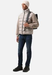 Pudret beige og grå jakke med høj krave, kombineret med mørkeblå jeans og sorte sneakers. Tilbehør: sort rygsæk og strikket hue.