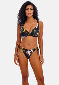 Černý květinový bikini, který obsahuje bralet s nastavitelnými ramínky a výztuhou, doplněný spodenky s vázáním po stranách. Živé květinové vzory kontrastují s látkou.