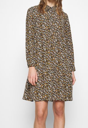 Mujer con vestido de manga larga hasta la rodilla, con un patrón floral denso en blanco, naranja y verde sobre un fondo oscuro.