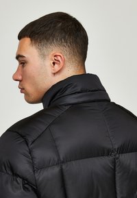 Svart boblejakke med høyt krage og kviltet mønster. Glatt stoff med en myk glans, designet for isolasjon og varme.
