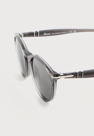 Στρογγυλά γυαλιά ηλίου με γκρι απόχρωση, διάφανο σκούρο γκρι πλαστικό σκελετό και ασημί μεταλλικά στοιχεία στους βραχίονες.