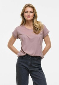 T-shirt à manches courtes et col rond en tissu mauve doux, associé à un jean en denim foncé. Texture lisse, coupe décontractée, manches repliées.