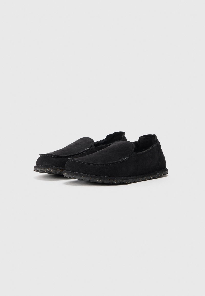 Mocasines de ante negro con perfil bajo, punta redondeada y diseño sin cordones. Suela texturizada con pequeños acentos antideslizantes. Sin marca visible.