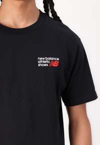 Czarna bawełniana koszulka z białym i czerwonym haftowanym logo na lewej stronie klatki piersiowej. Krótkie rękawy i okrągły dekolt.