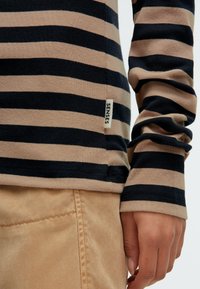 Gestreiftes Langarmhemd in Schwarz und Beige, mit taillierter Passform und einem kleinen Etikett mit "SENSES" nahe dem Saum. Weiche Textilstruktur.