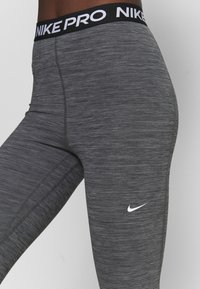 Leggings Nike Pro in grigio melange con una fascia nera in vita, caratterizzati da testo bianco "NIKE PRO" e un logo bianco sulla gamba. Texture liscia.