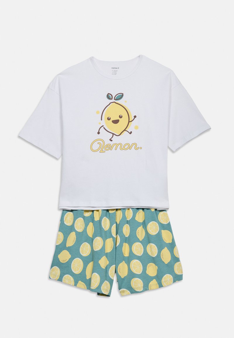 Λευκό τοπ με κοντά μανίκια, με γραφικό χαμογελαστού λεμονιού και τη λέξη «Lemon», σετ με μπλε σορτς με κίτρινα μοτίβα φέτες λεμονιού.