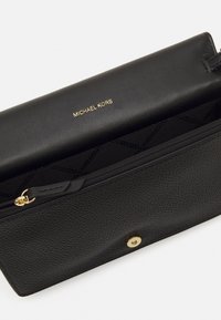 Black textured leather wallet with gold lettering "MICHAEL KORS" on the front, featuring a zip closure and snap button detail.