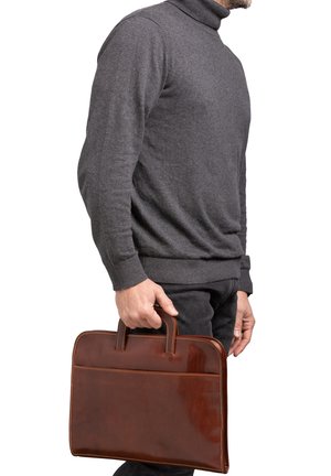 Una valigetta in pelle marrone con texture liscia, doppi manici e una cucitura decorativa. Tenuta da una persona con un maglione a collo alto grigio e pantaloni scuri.