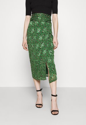 Jupe midi verte à imprimé léopard noir et beige, fente à l'avant, portée avec un haut noir à manches courtes et des talons noirs à bride cheville.
