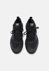 Czarne buty sportowe z teksturowanymi siateczkowymi cholewkami, płaskimi sznurowadłami i kontrastującą gumową podeszwą. Zawierają logo na języku oraz subtelne akcenty wzór.
