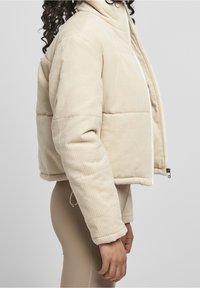 Beige cordjakett i ribbstickad sammet med hög krage, quiltad textur och vit dragkedja. Har ribbade manschetter och dragsko i nederkant.