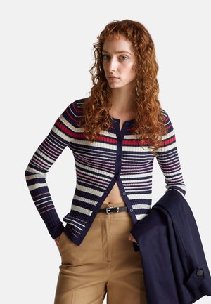Knopen-up cardigan met marineblauwe, rode en crèmekleurige strepen, ribbelstructuur en een korte snit. Gecombineerd met tan hoge taille broeken.