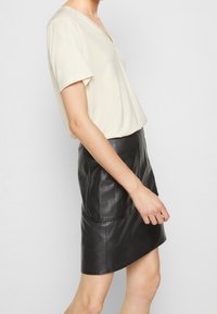 Krämfärgad t-shirt med v-ringning och korta ärmar, tillsammans med en figurnära svart läder minikjol med slät yta och subtila sömmar.