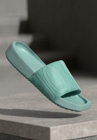 Aqua slide sandal lavet af gummi med en bred rem, der har præget bølgemønstre og en tekstureret sål for godt greb.