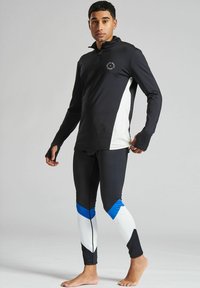 Långärmad svart och vit sporttop med kvartzip och platta sömmar, ihopparad med svarta leggings som har blå och vita geometriska mönster.