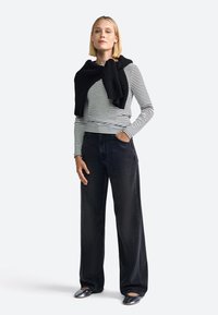 Sorte brede jeans parret med en sort og hvid stribet langærmet skjorte og en sort striktrøje draperet over skuldrene. Sølvfarvede sko.